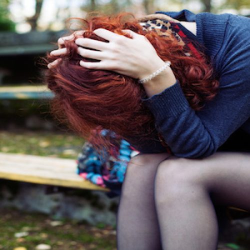 Ginger woman sitting in despair on the bench in the park, head in the hands